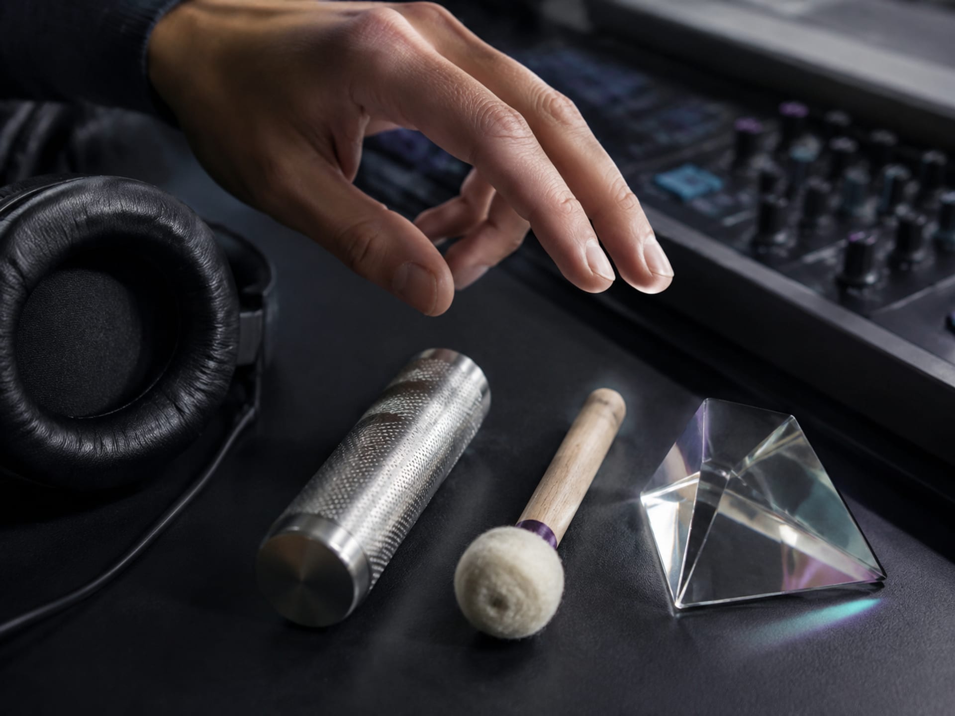 Auriculares junto a un shaker metálico, un martillo de piano de fieltro y un prisma de vidrio que representan texturas sonoras contrastantes