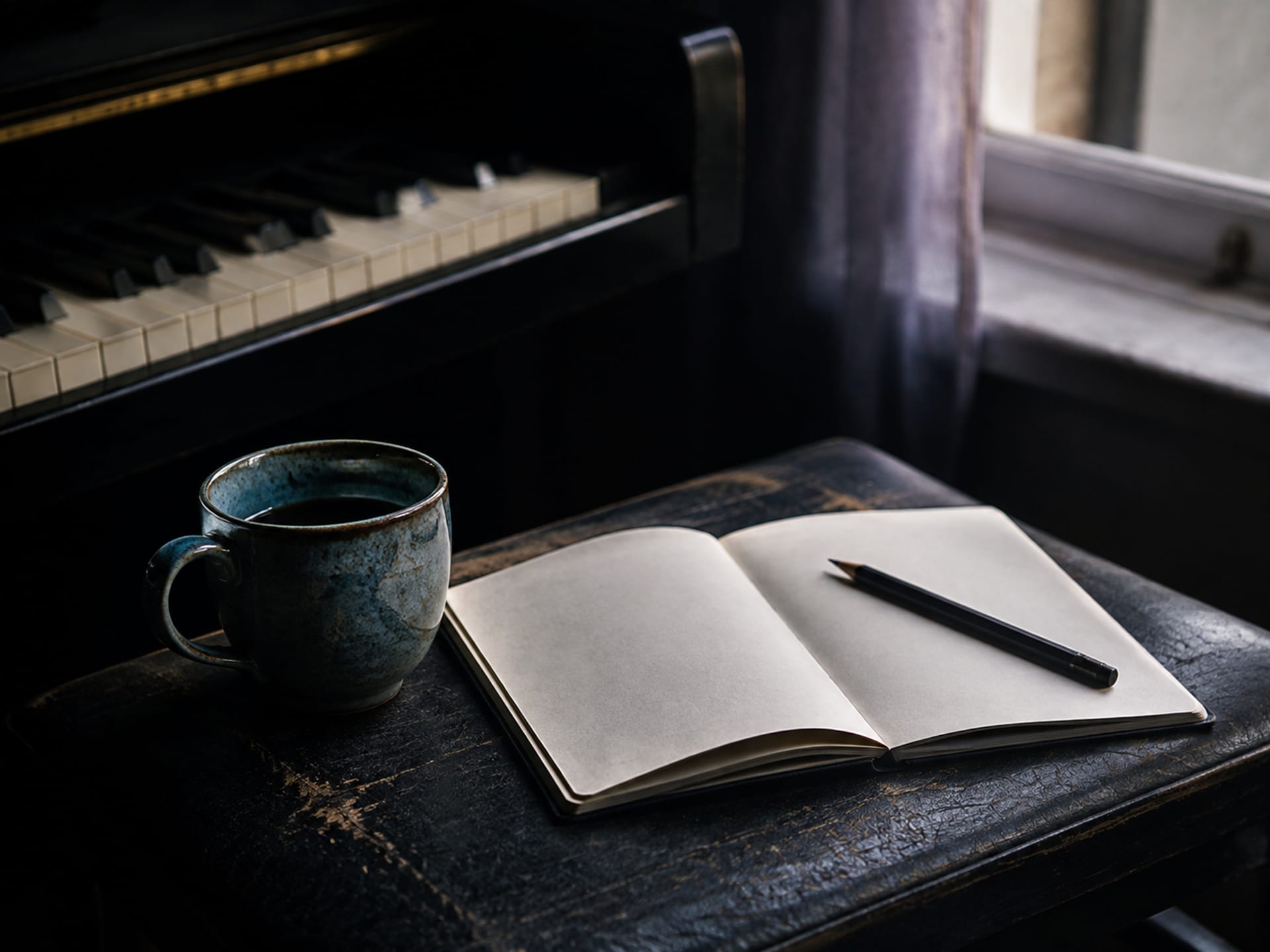 Een blauwe keramieken kop en een leeg notitieboek naast pianotoetsen als inspiratie voor een persoonlijk herdenkingslied