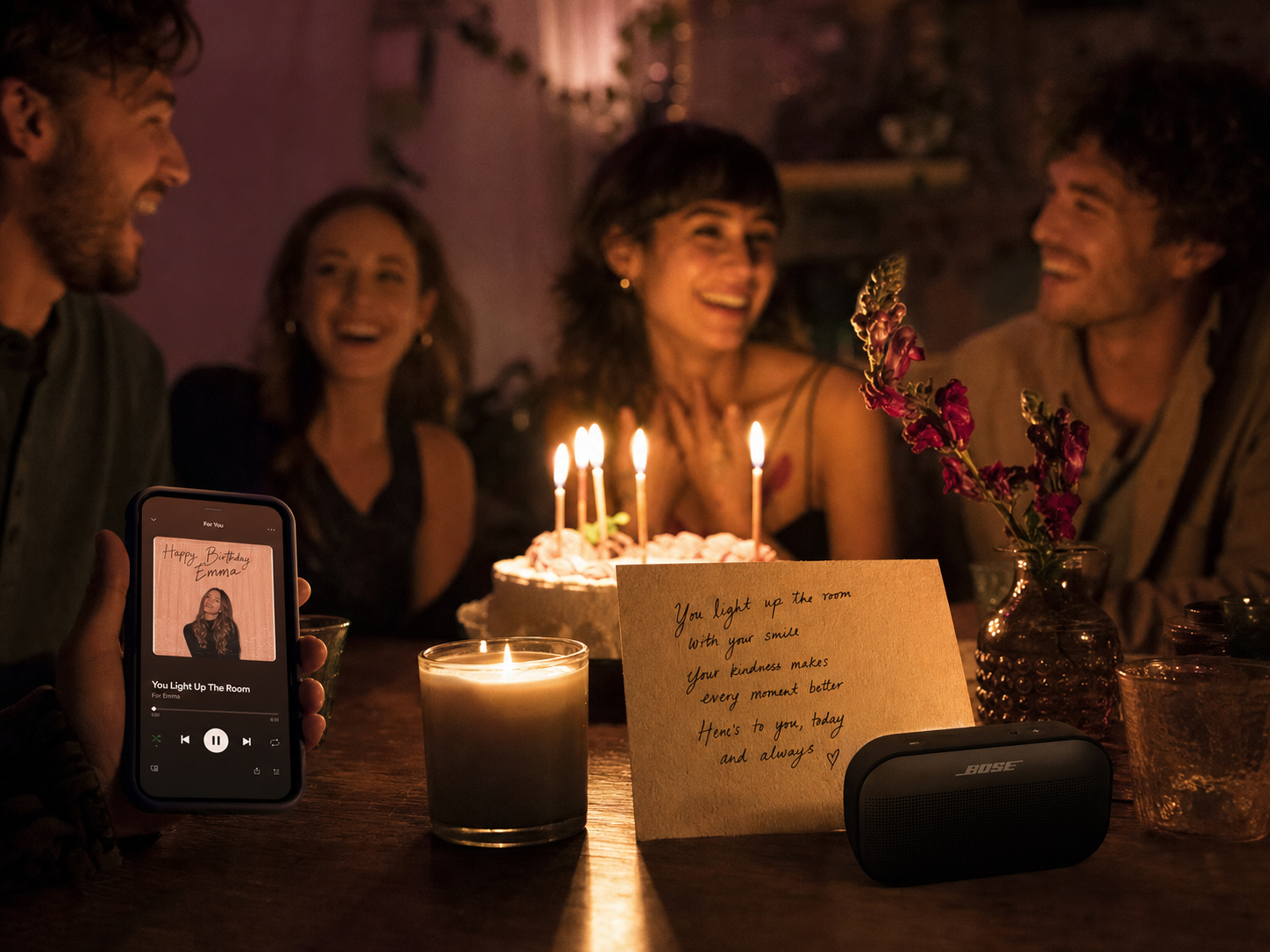 Birthday table with a phone playing a personalized song while friends react to lyrics about the guest of honor